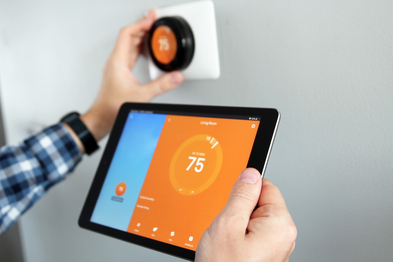 a man adjusting the temperature on thermostat using a tablet with a smart home app