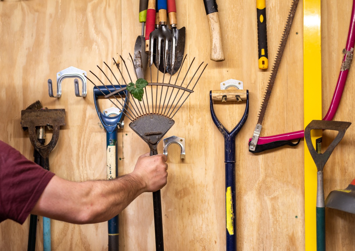 a man hanging gardening tools at the wall-mounted hooks in the garage