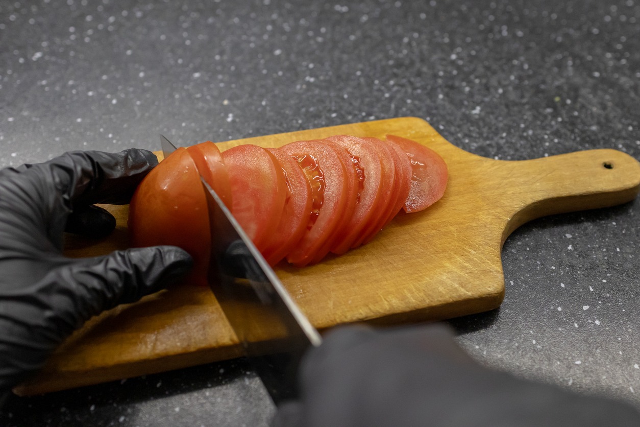 Slicing fresh tomato on wooden cutting board