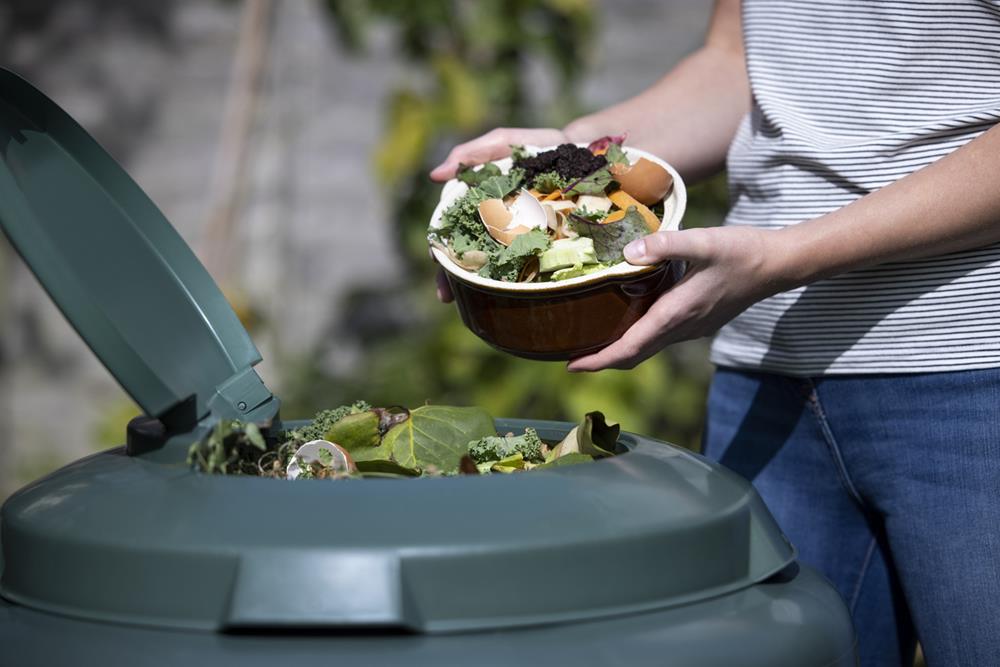 Woman emptying food waste into garden composter at home