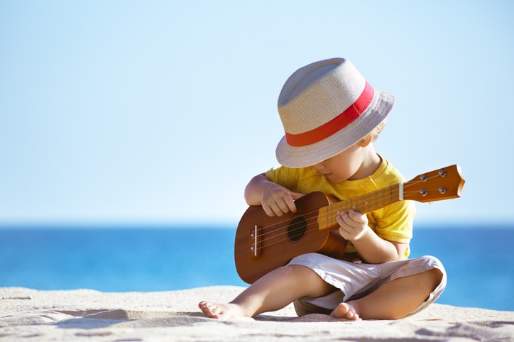 Little boy plays guitar ukulele at sea beach