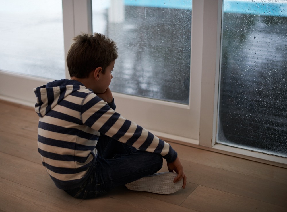Rainy days with nothing to do...A young boy sitting by the window and looking bored while it rains outside.